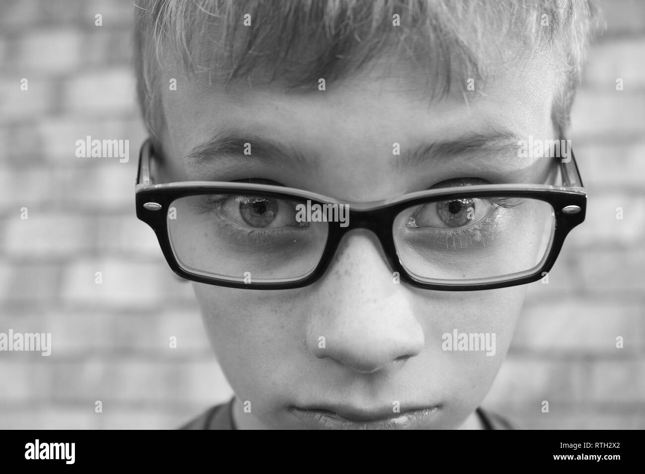 Black and white macro shot of upset preteen boy wearing glasses Stock Photo