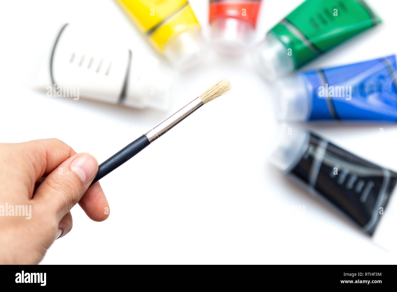 Man holding paint brush over colored paint tubes Stock Photo
