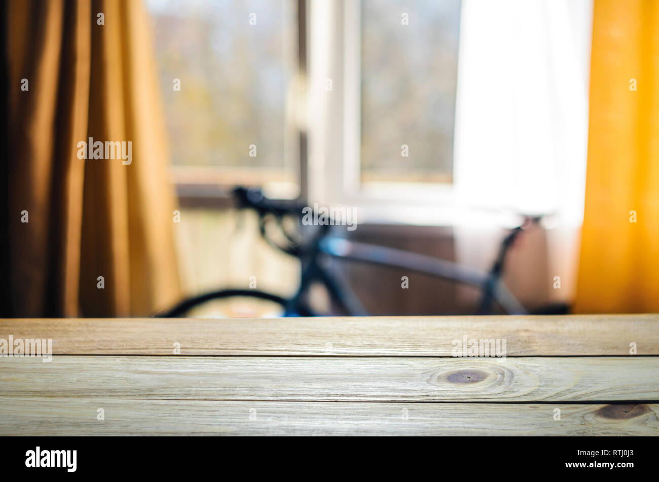 Product Placement Background. Wooden Table Against Blurry Interior of Cyclist's Living Room with Large Window and Blue Sport Bicycle Stock Photo