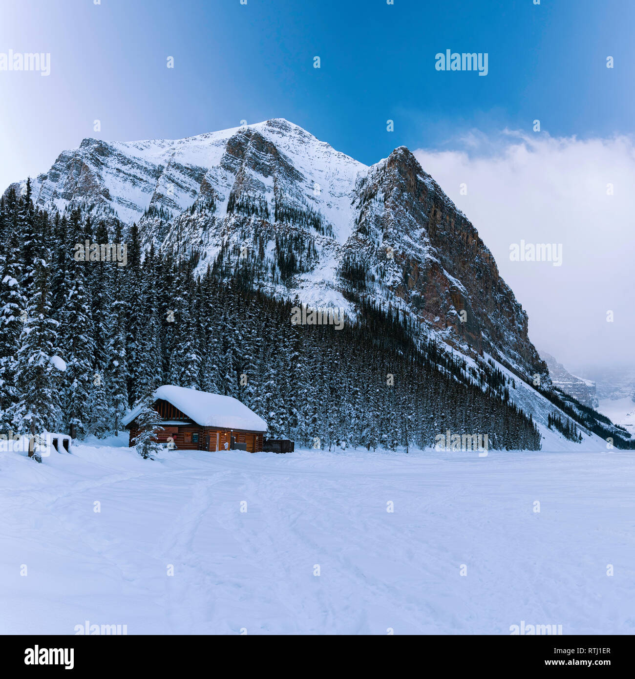 Log cabin on the shore of a frozen, snow covered Lake Louise with Fairview Mountain behind, Banff National Park, Canadian Rockies, Alberta, Canada Stock Photo