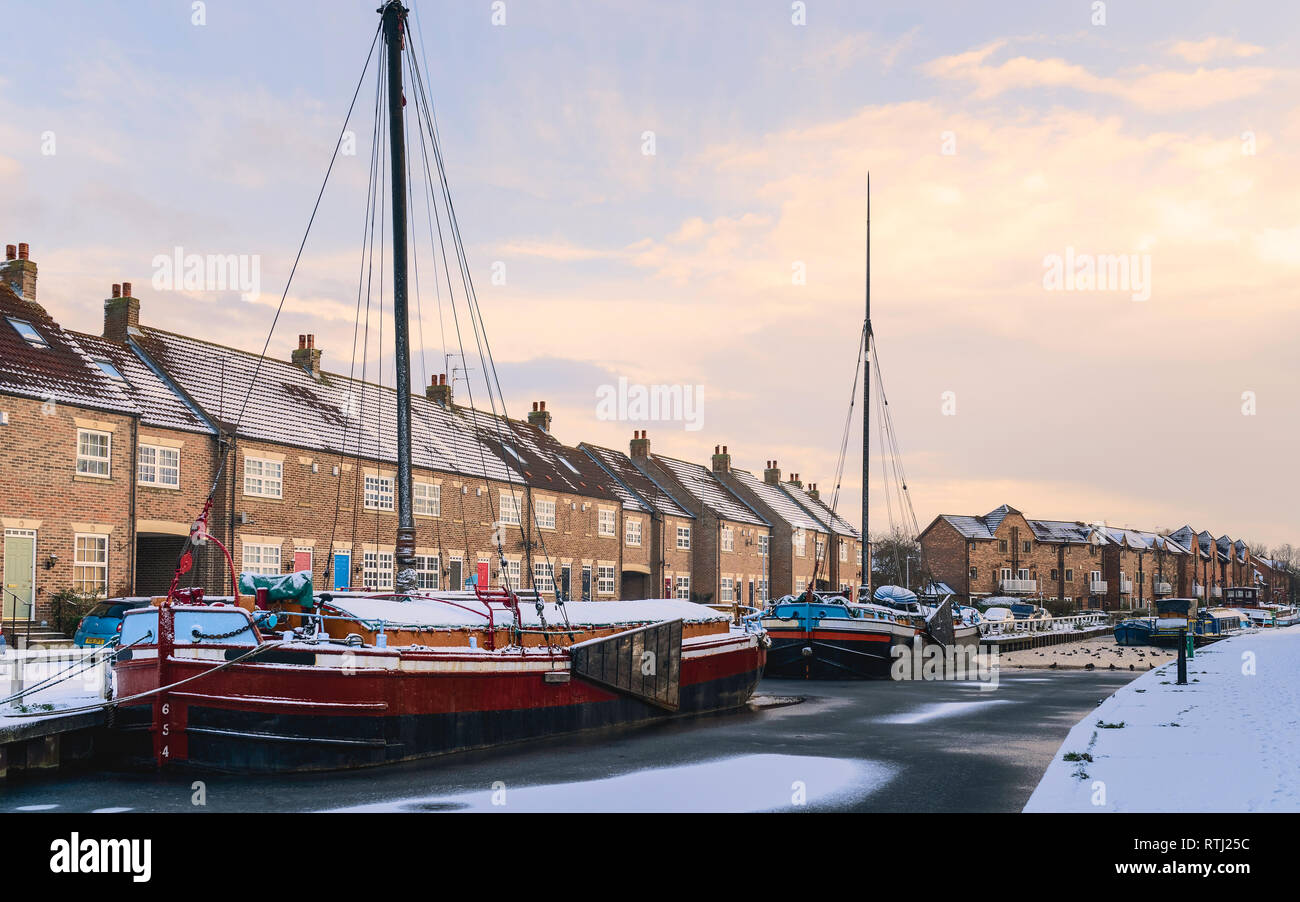 Vintage barges moored along the frozen beck (canal) and covered in snow flanked by town houses on a cold winter morning in Beverley, Yorkshire, UK. Stock Photo
