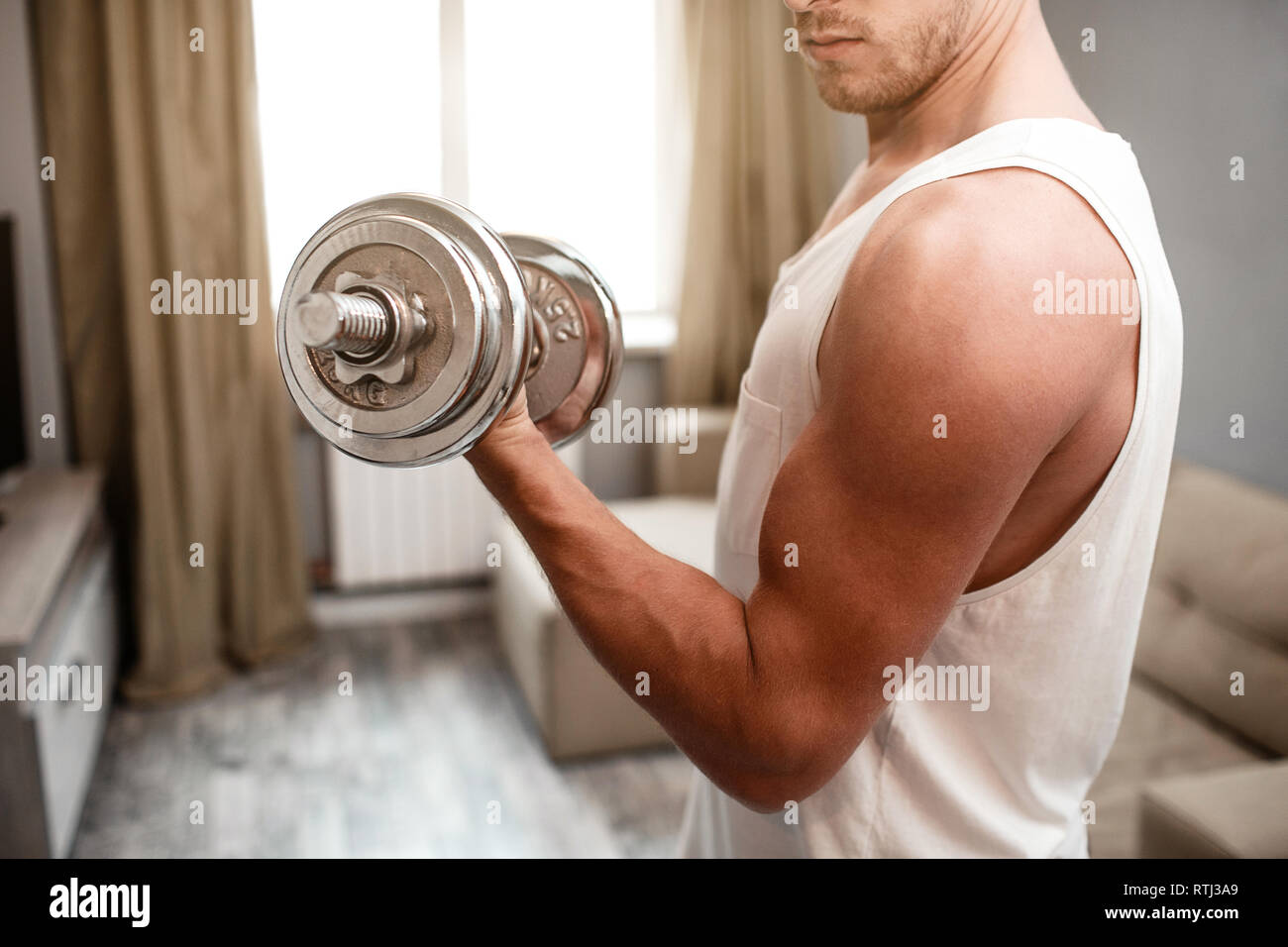 Young wellbuilt man go in for sports in apartment. Cut view of guy