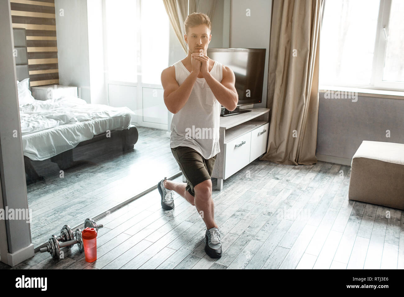 Young wellbuilt man go in for sports in apartment. Squat on one knee