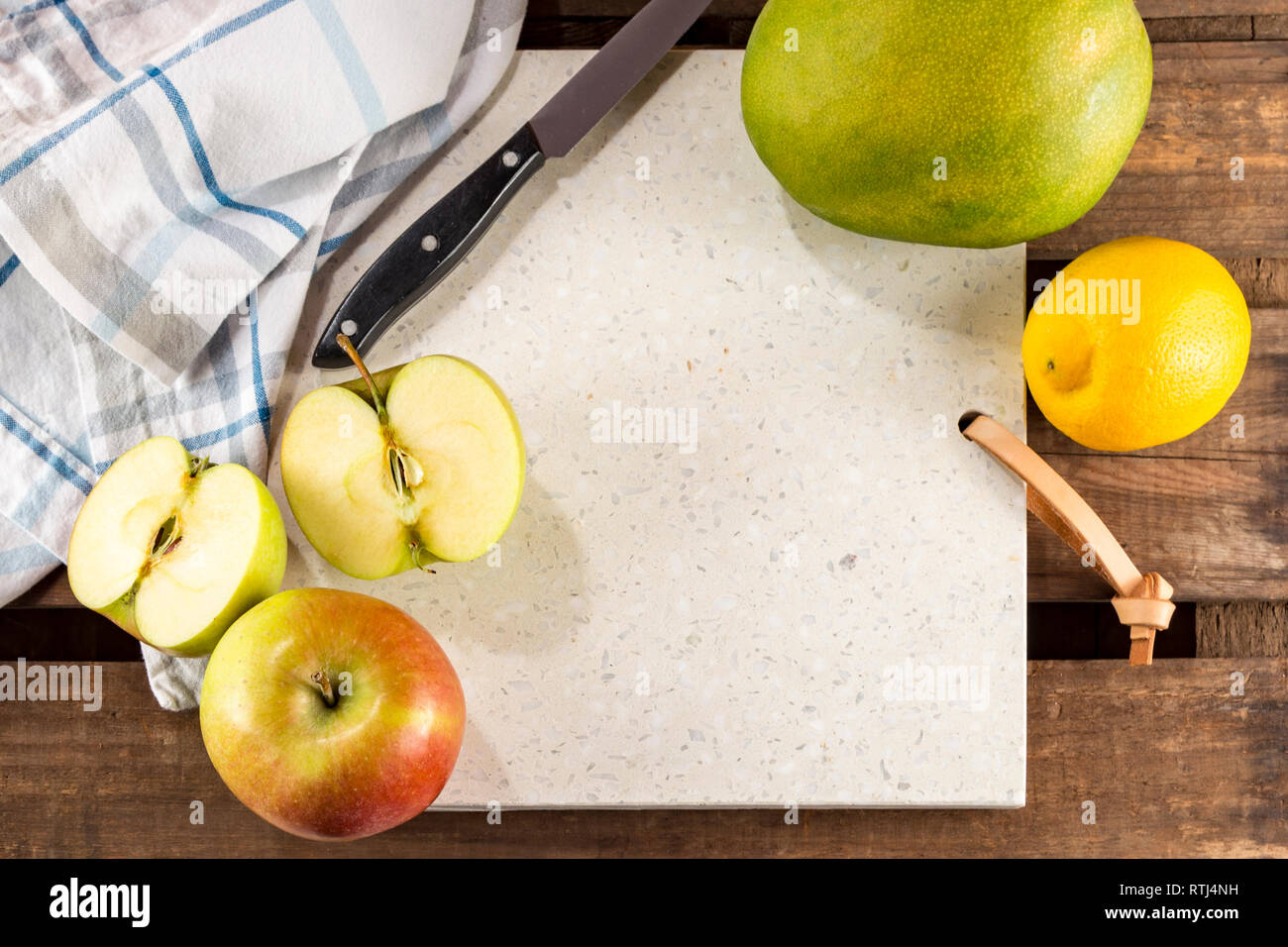 Concrete stone server with space for text on rustic wood plank surface. Arranged apples, lemon and mango, knife and cloth. Top view, flat lay. Stock Photo