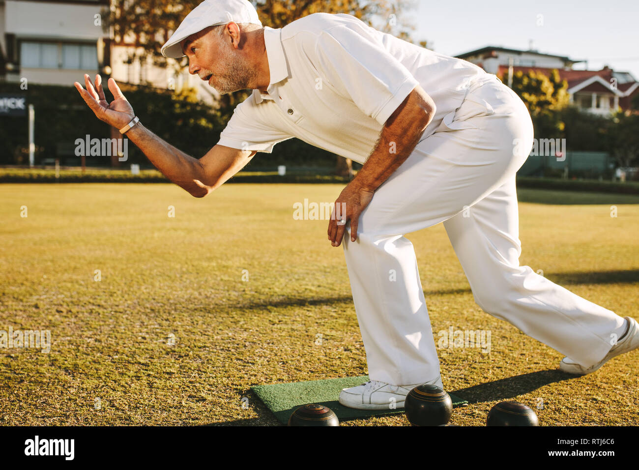 Elderly man playing a game of boules. Senior man in hat throws a boules standing in position in a lawn. Stock Photo
