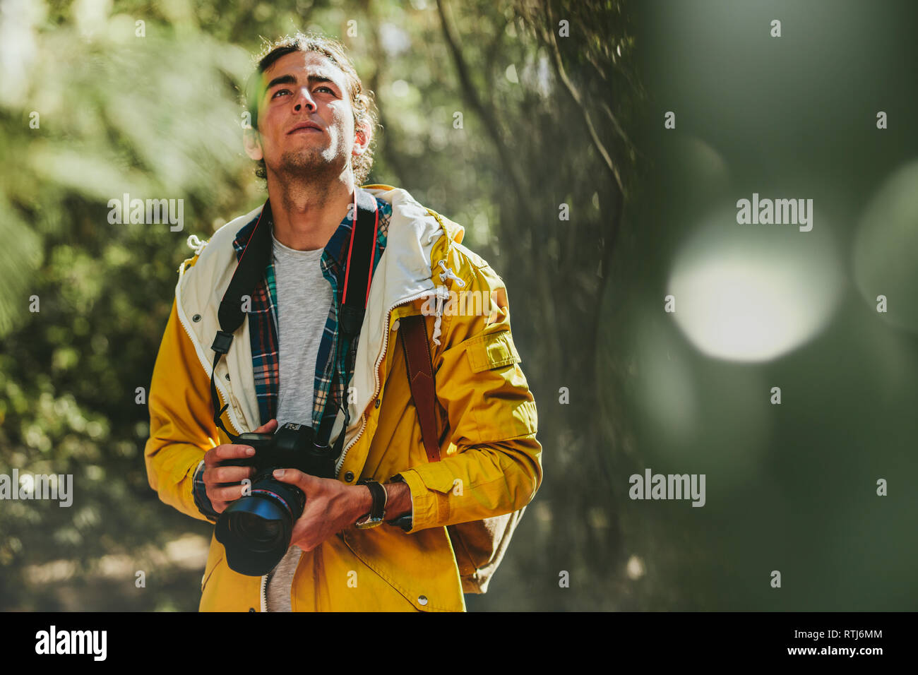 Portrait of a man wearing jacket and backpack walking in a forest holding a dslr camera. Man exploring a forest capturing the beauty in a digital came Stock Photo