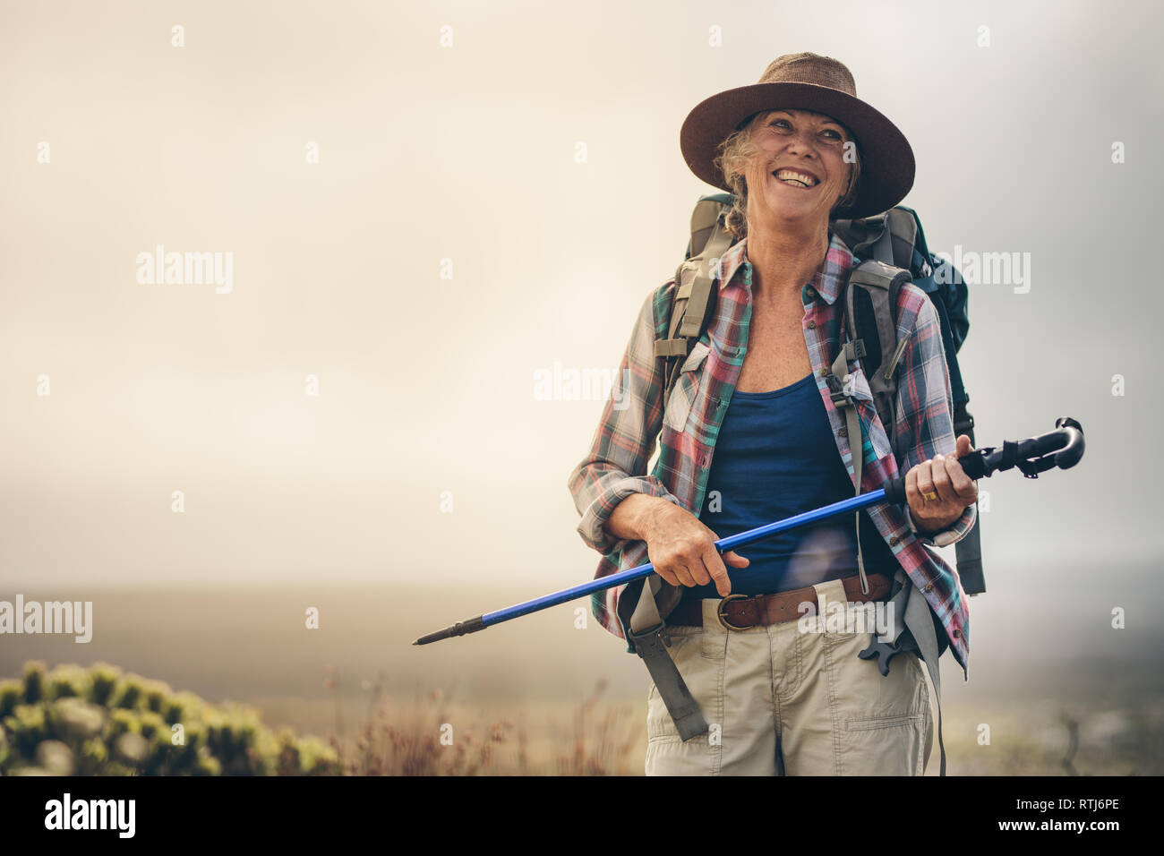 Portrait of a smiling woman hiker walking holding her hiking pole. Close up of a woman wearing hat and a backpack in a cheerful mood during her trekki Stock Photo