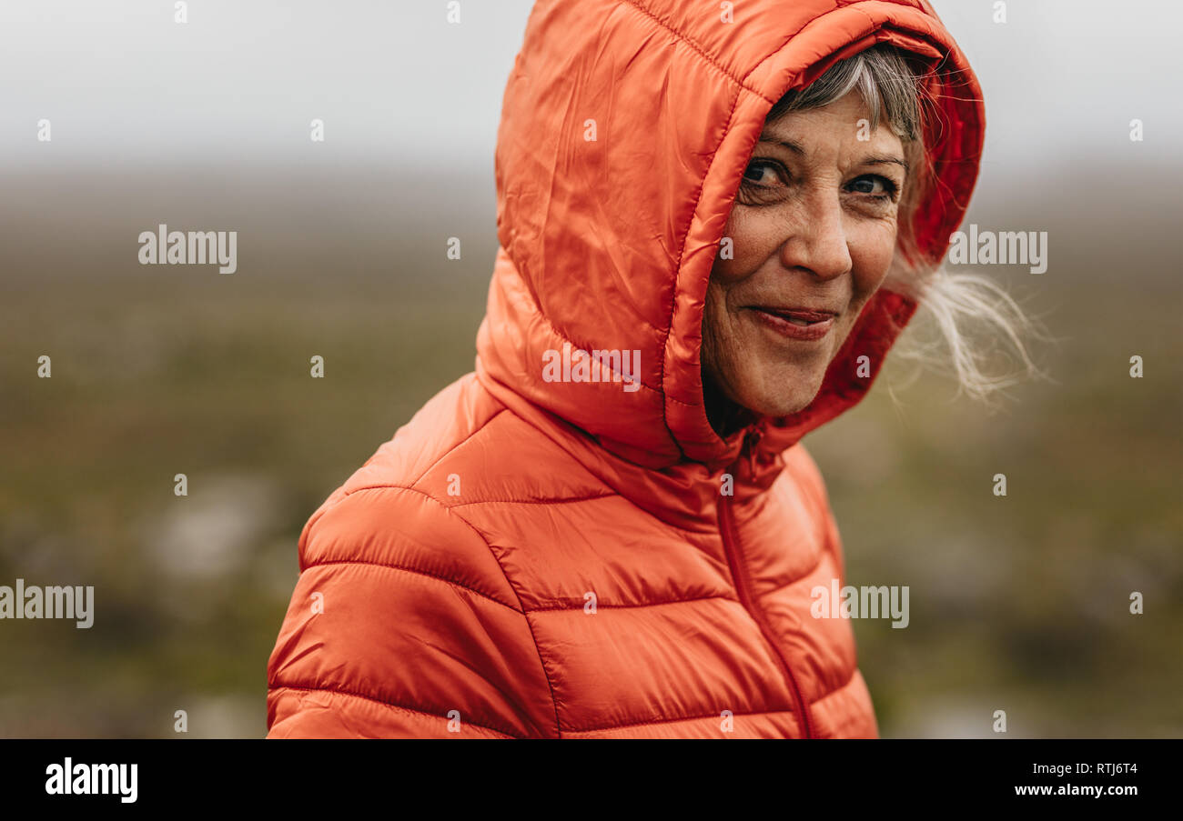 Close up of a smiling senior woman in a hooded jacket. Senior woman with a beautiful smile standing outdoors. Stock Photo