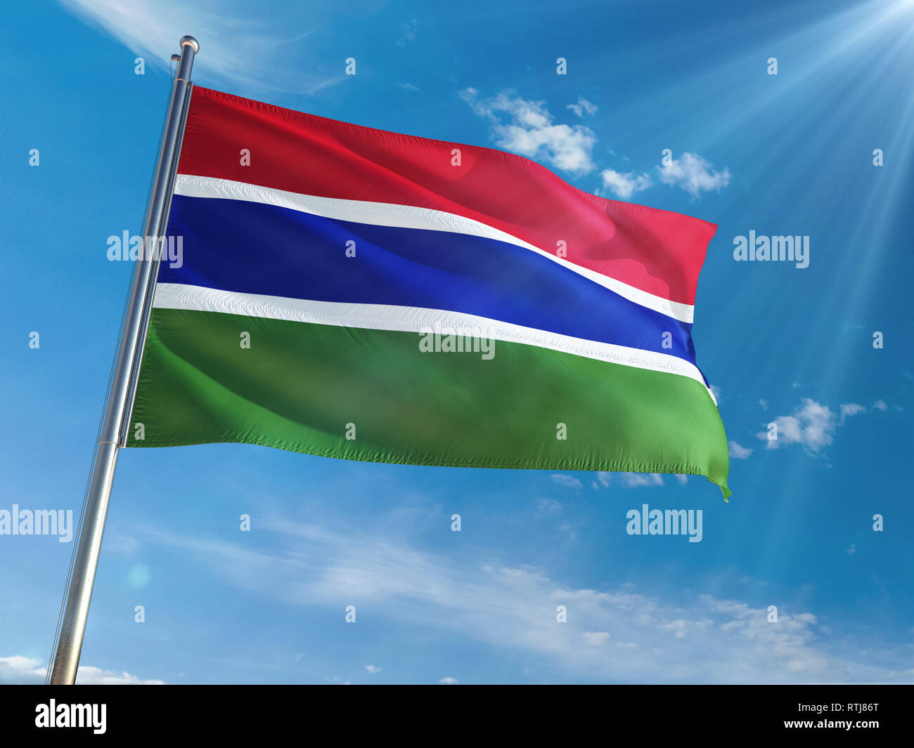 Gambia National Flag Waving on pole against sunny blue sky background ...