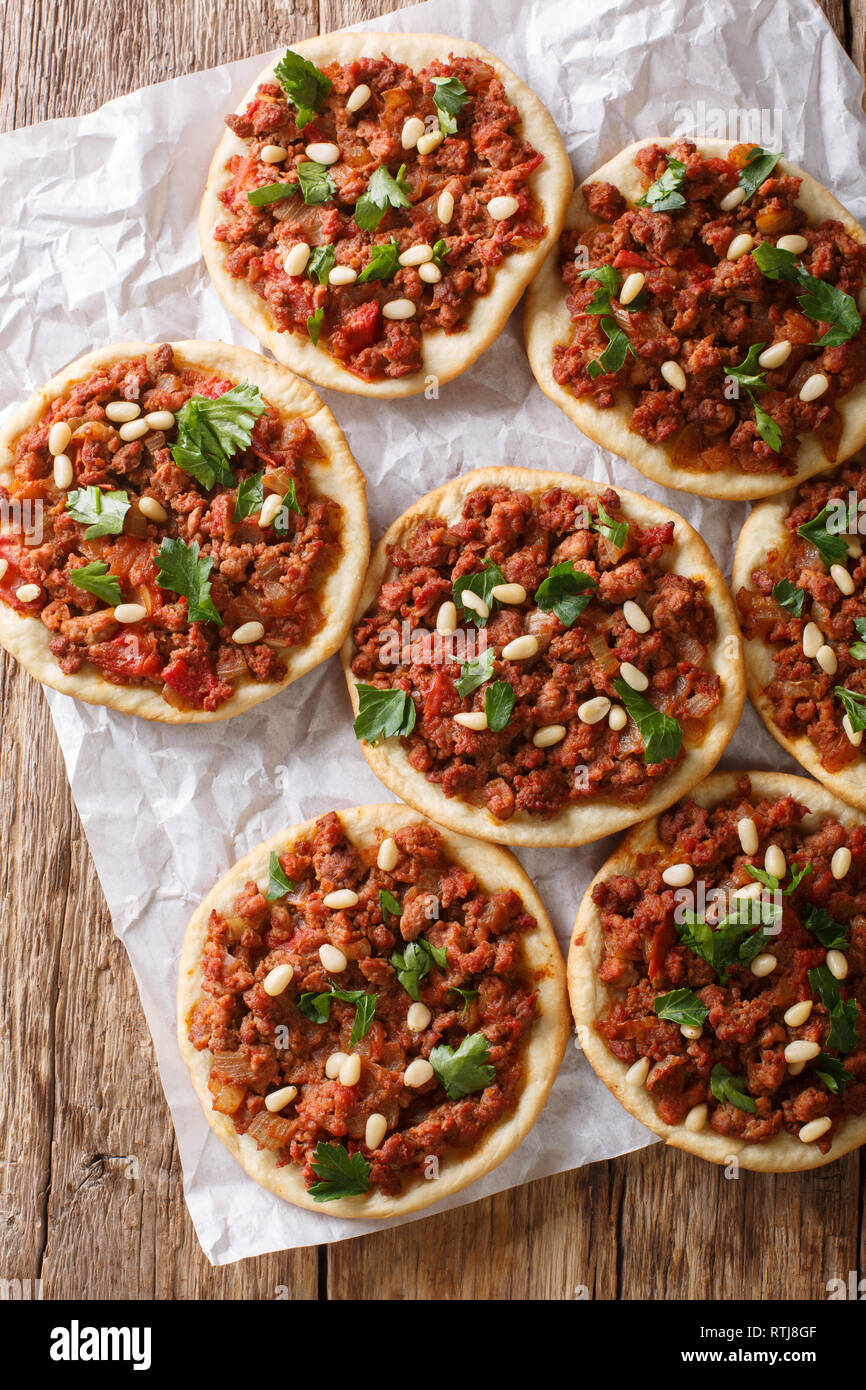 Arab mini pizza with minced meat, tomatoes, onions, spices and pine nuts closeup on the table. Vertical top view from above Stock Photo