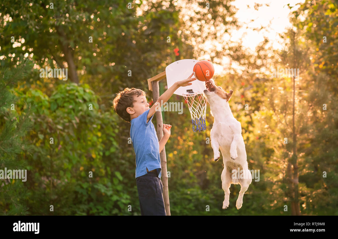 Kid playing basketball with his dog in backyard garden Stock Photo