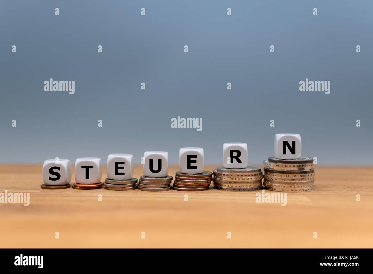Dice form the German word 'STEUERN' ('TAX' in English) on top of stacks of coins.  Concept of increasing taxes. Stock Photo