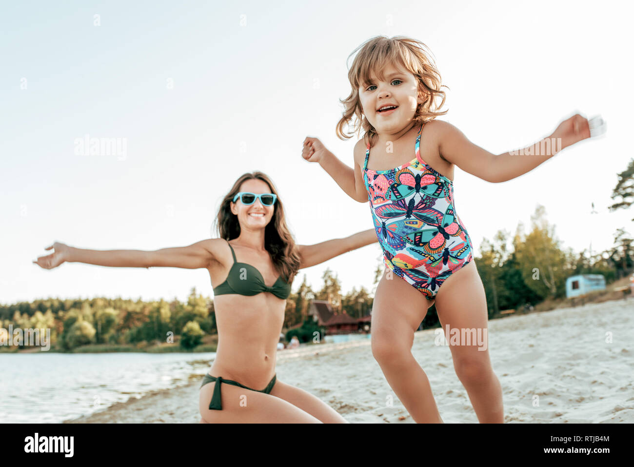 Little girl 2-5 years old, playing with a young mother on the beach in  summer, outdoor resort by the lake. Happy rest on the weekend. Bright  swimsuit Stock Photo - Alamy
