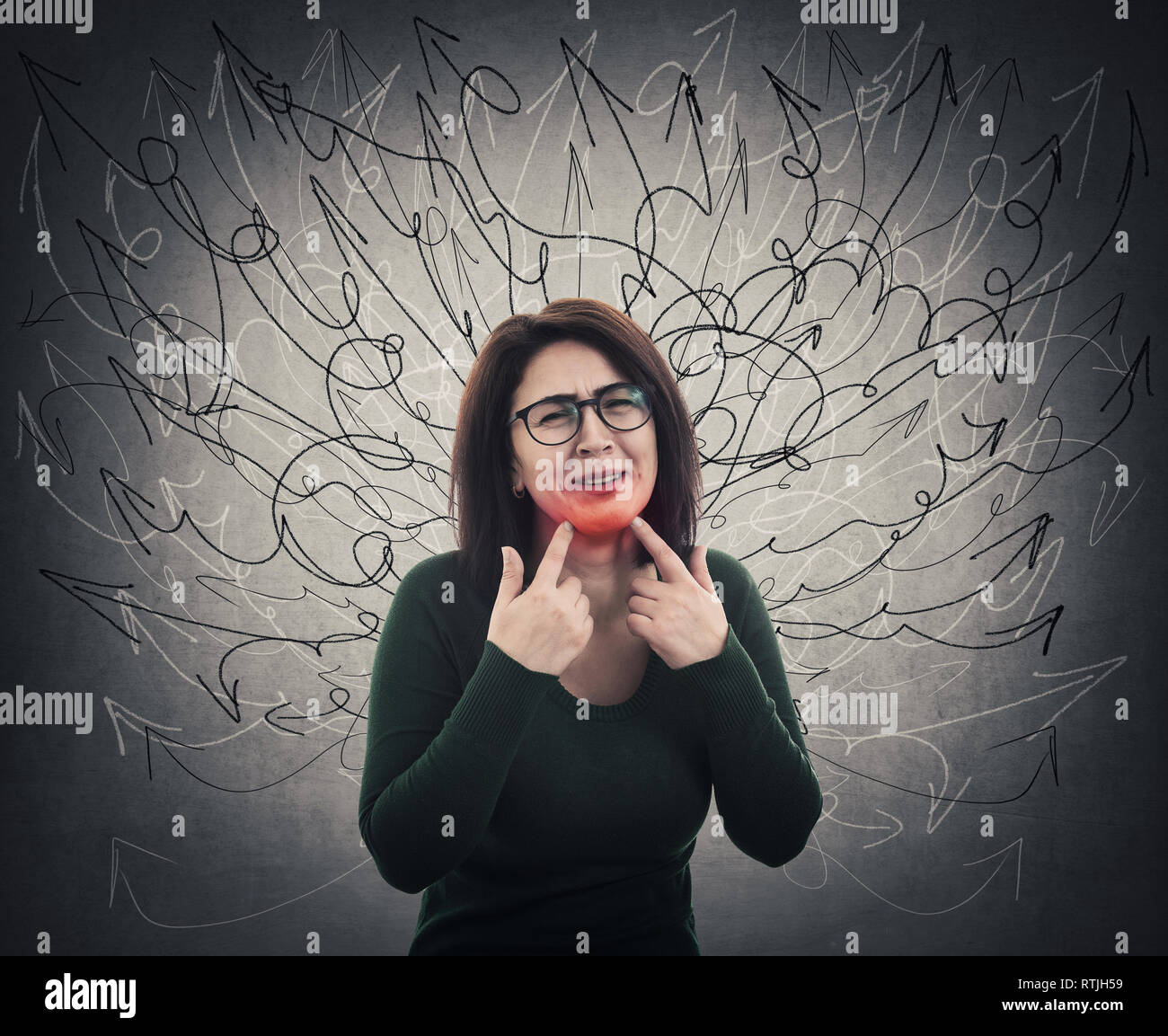 Young woman suffering from toothache. Teeth pain problem, girl pointing fingers to sore gums over grey wall. Dental health and care concept. Sad emoti Stock Photo