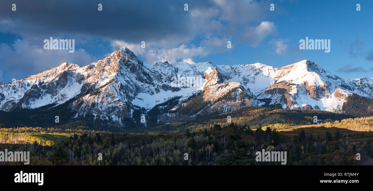 Mount Sneffels is within the Uncompahgre National Forest. An early fall snowstorm covers the mountain range  with aspen groves in full color. Stock Photo
