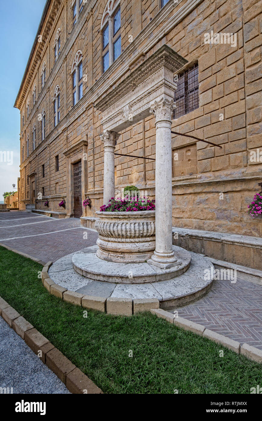 Old well in the main square of Pienza. The travertine well of the Rossellino and the front of Palazzo Piccolomini in Pienza, Tuscany, Italy Stock Photo