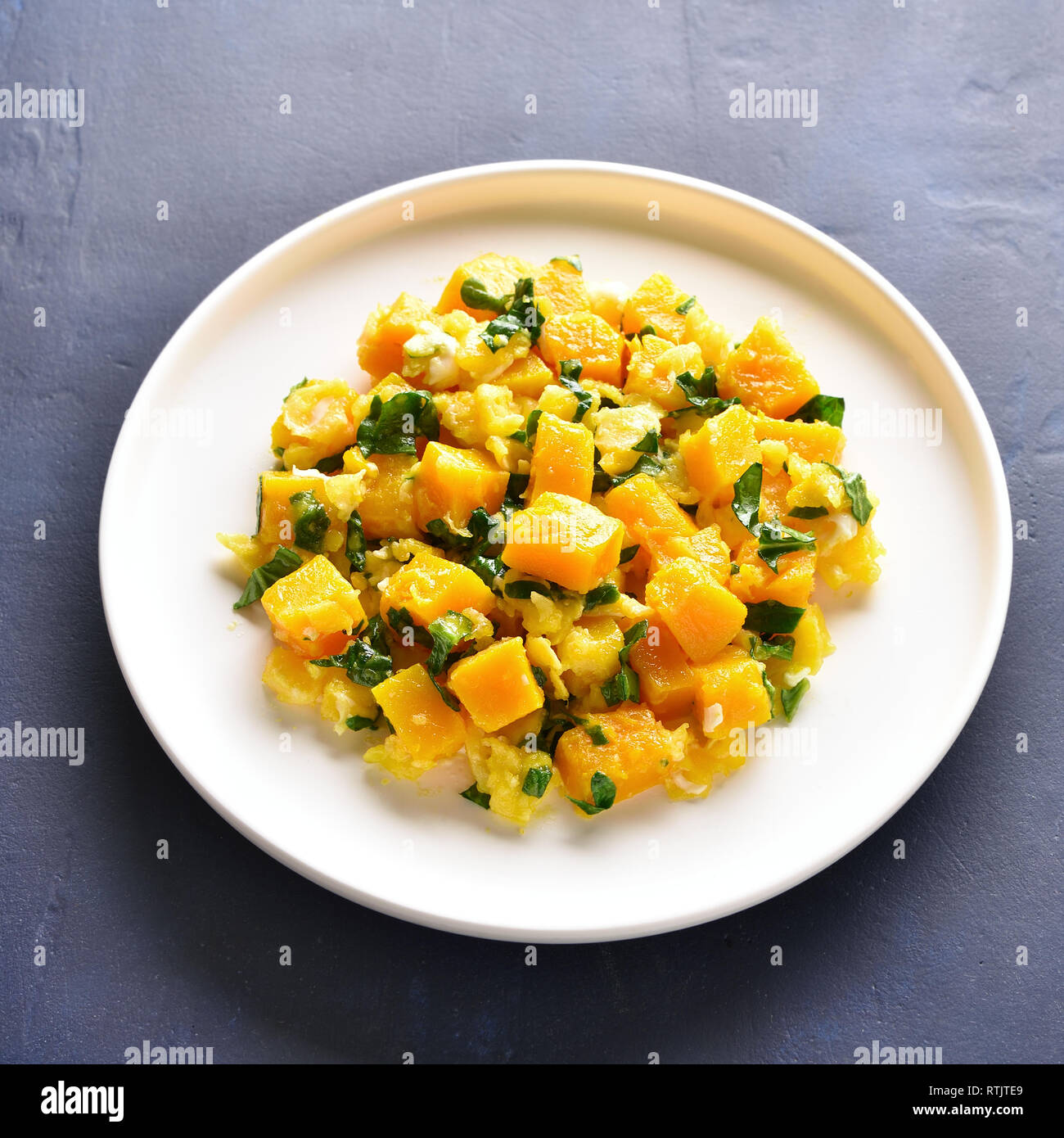 Stirfried pumpkin with eggs on plate over blue stone background. Pumpkin and egg stir fry in