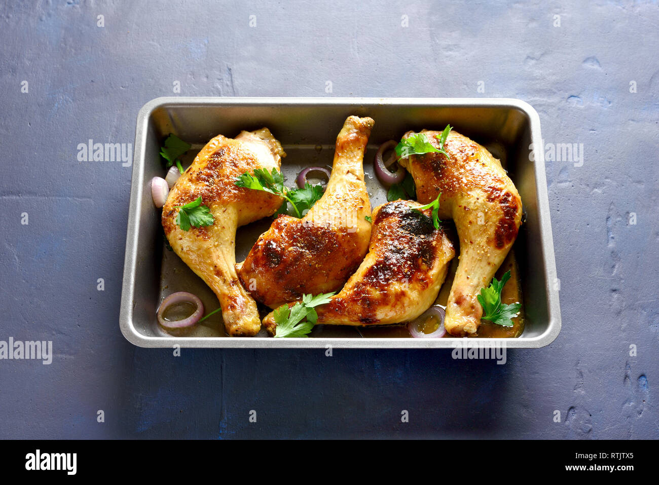 Baked chicken legs in baking tray on blue stone background Stock Photo
