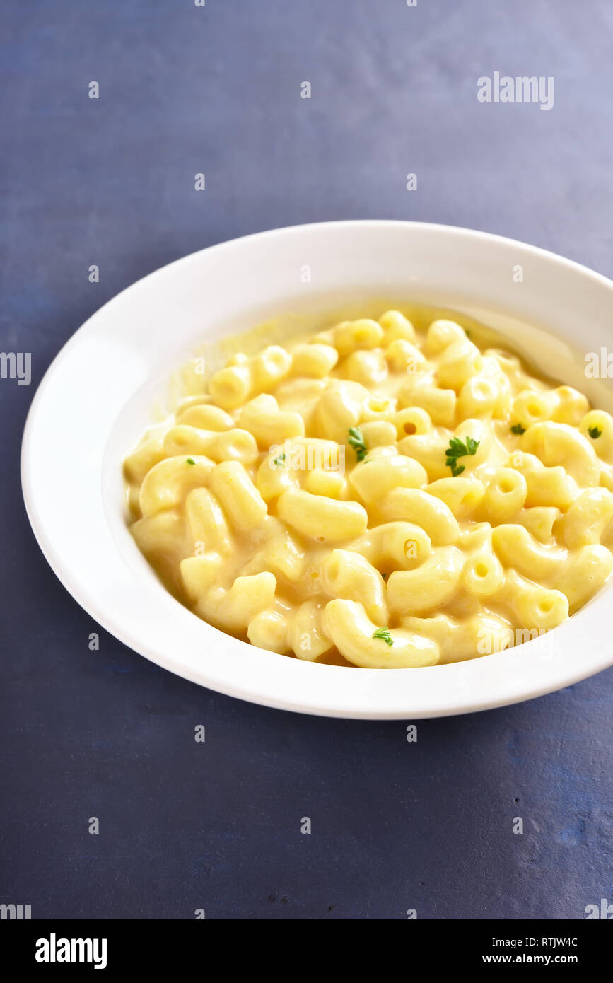Close up of macaroni and cheese in white bowl on blue stone background. Stock Photo