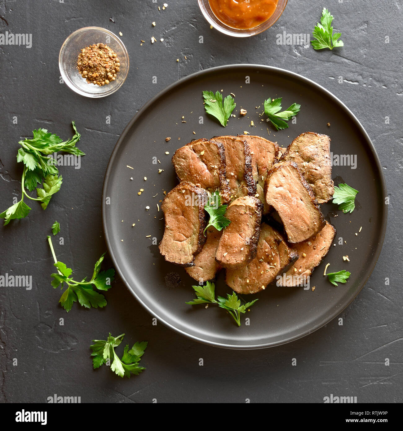Grilled sliced beef liver on plate over black stone background. Cooked