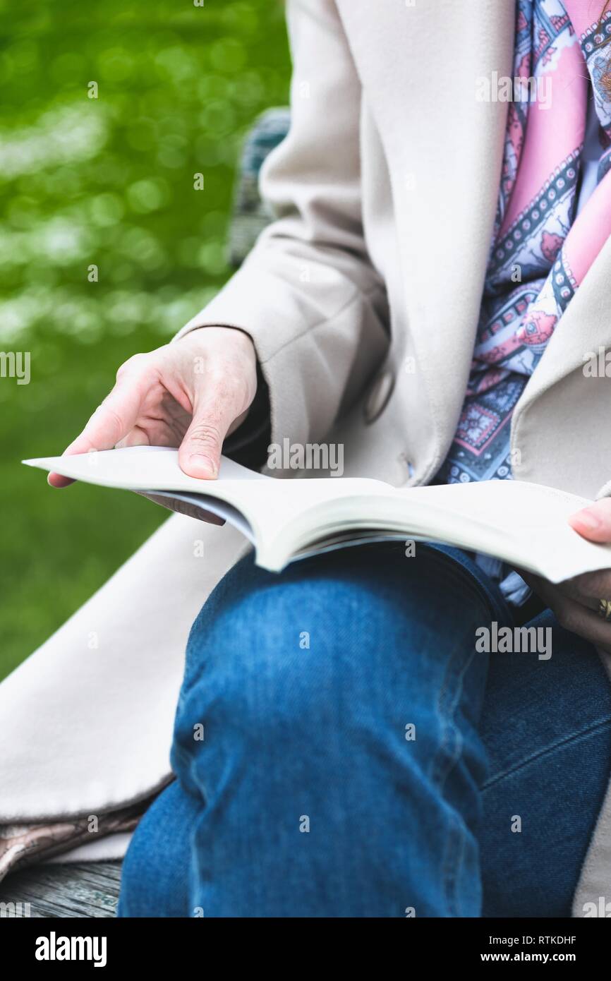 the girl is sitting on a park bench and reading a book Stock Photo - Alamy