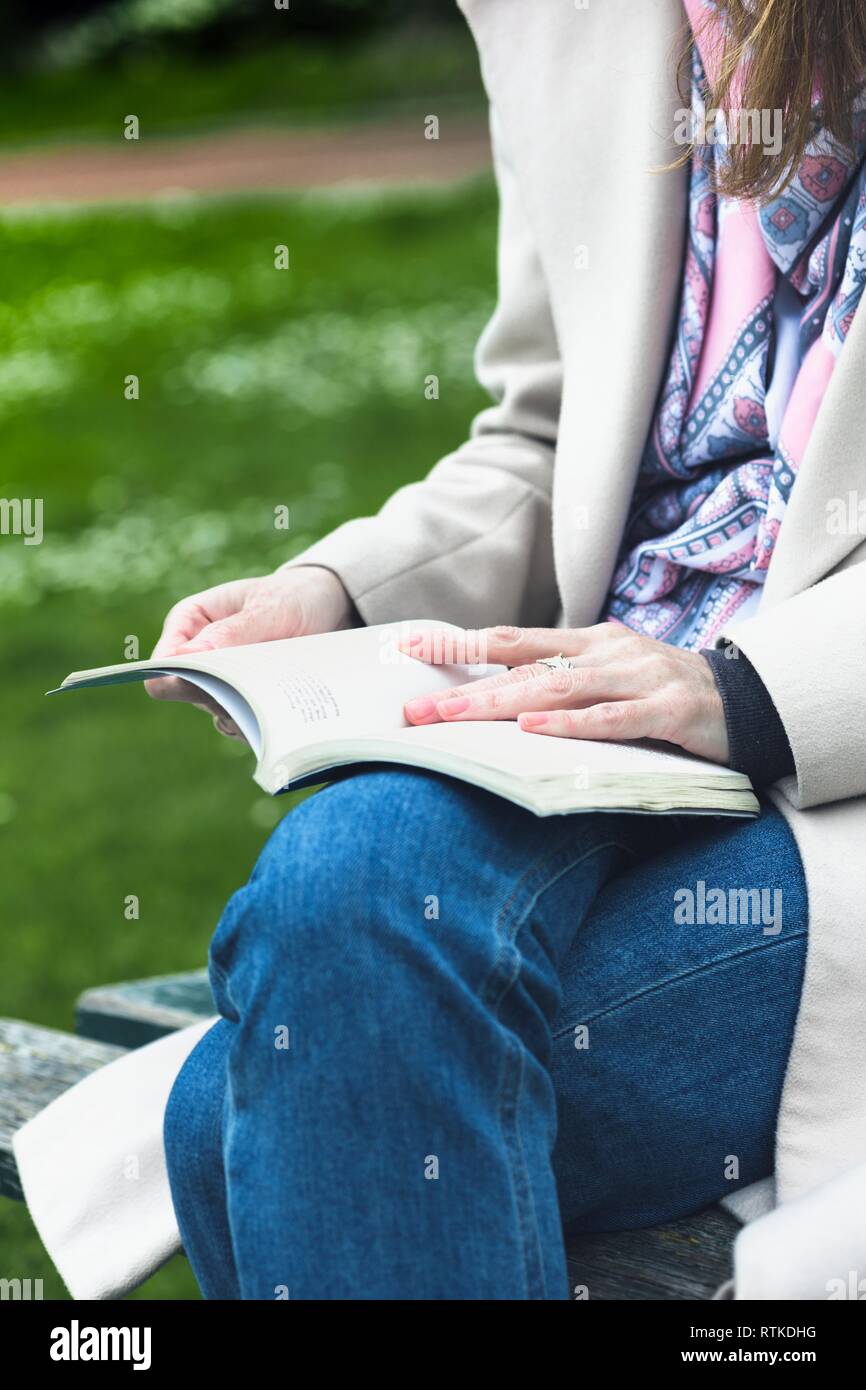 the girl is sitting on a park bench and reading a book Stock Photo - Alamy