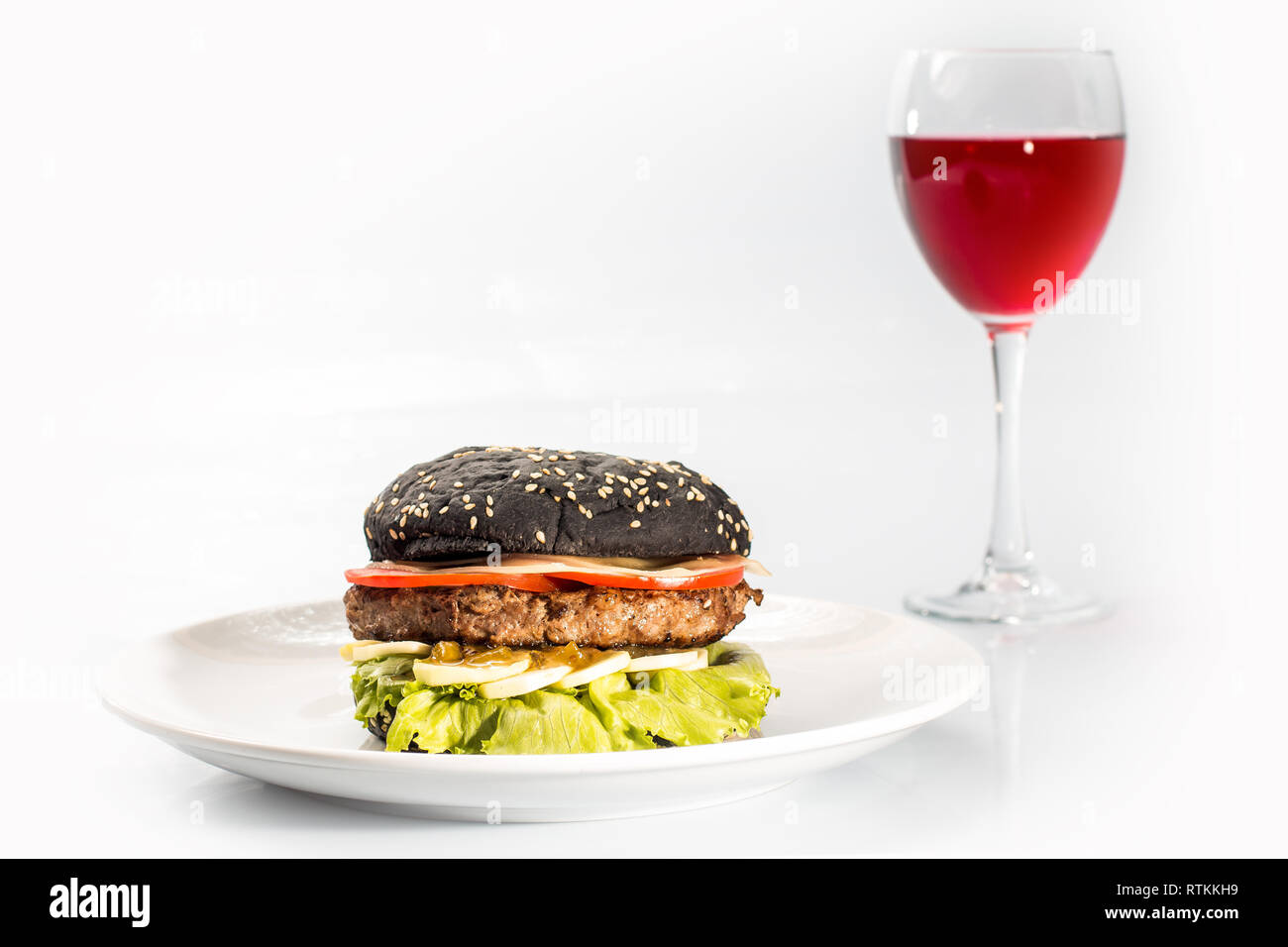 cheeseburger with black bread, beef cutlet, bacon, tomatoes and cheese slices, seasoned with sauce and green salad for a restaurant menu on a white is Stock Photo