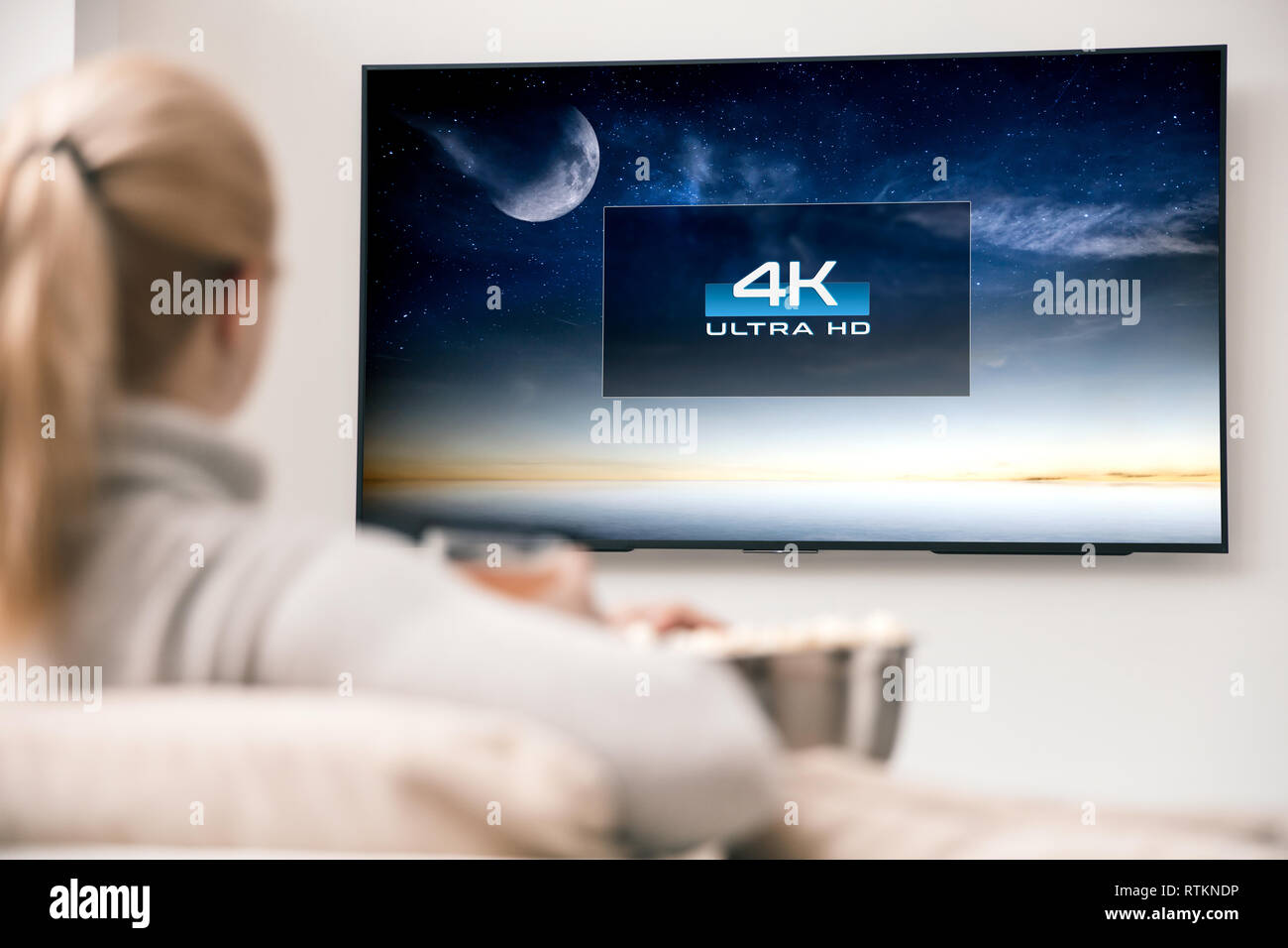 Woman watches tv with 8k ultra hd resolution. Picture on the screen created in graphic software. Stock Photo