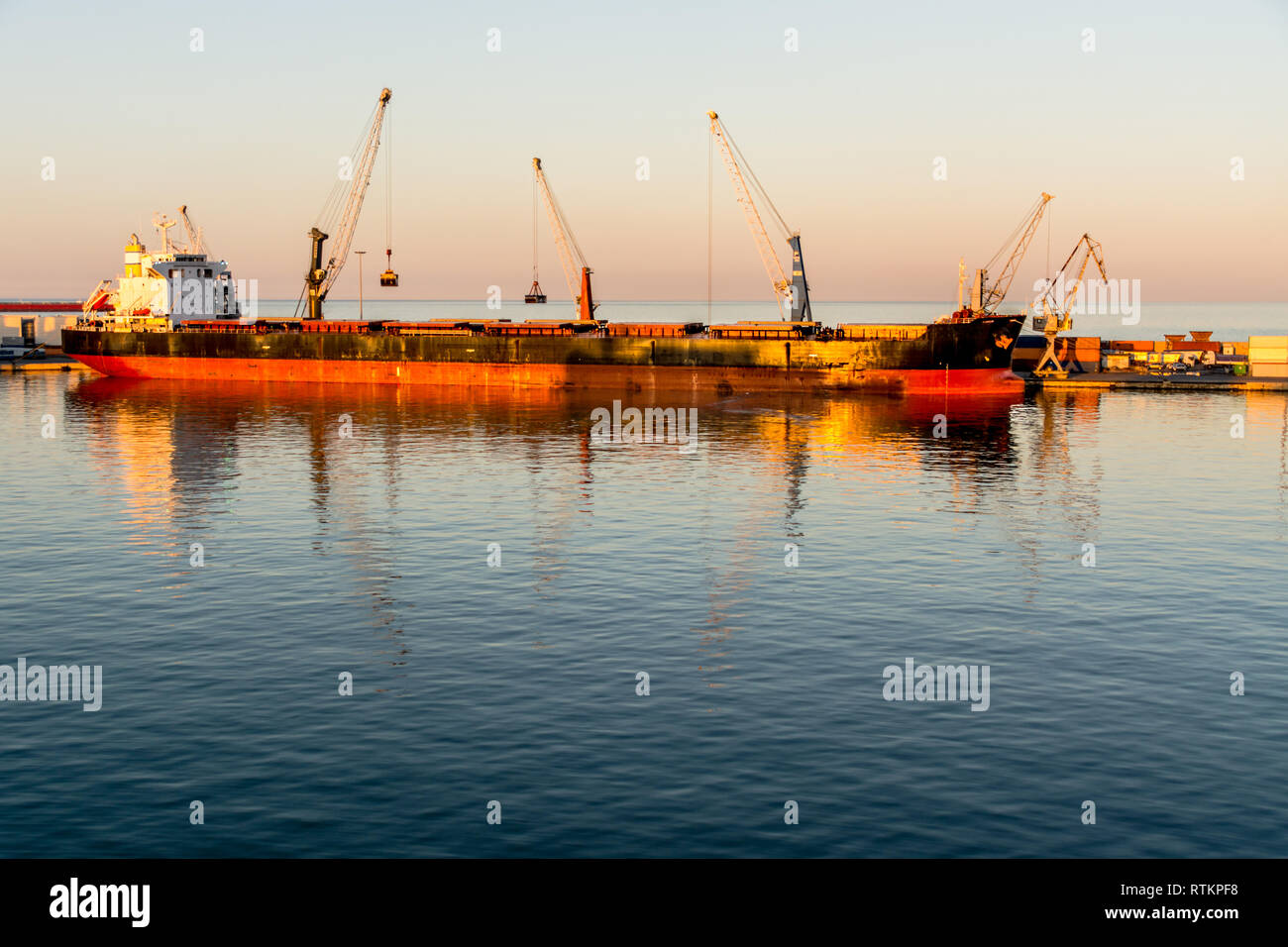 A cargo ship docks in the port, surrounded by an array of towering cranes and vividly colored containers ready for loading and unloading. Stock Photo