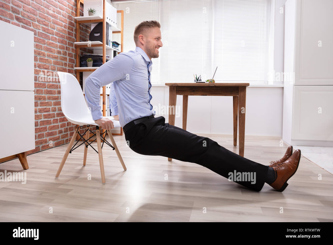 Happy Young Businessman Doing Triceps Dips In Office Stock