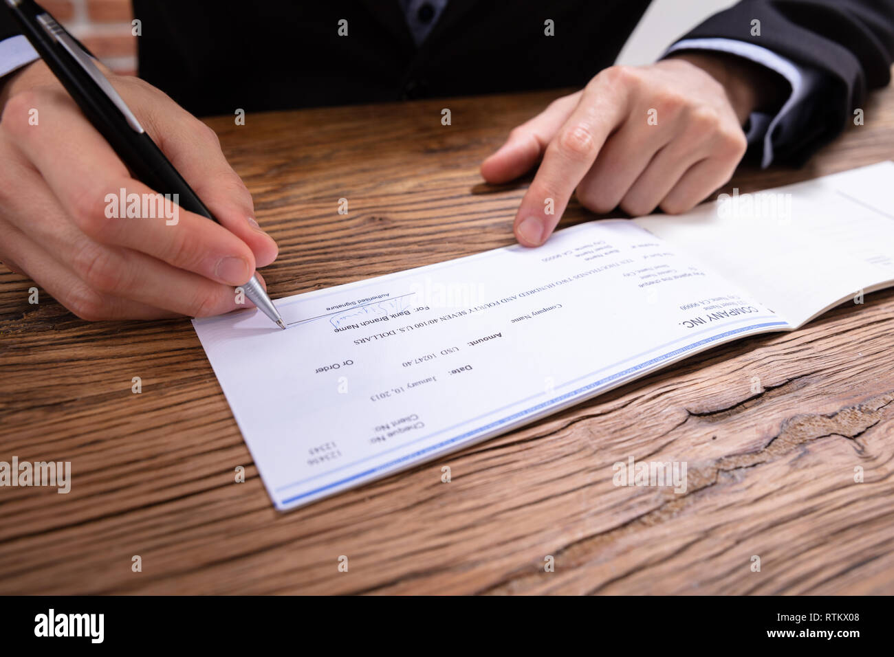 Close-up Of A Businessperson's Hand Signing Cheque With Pen In Office Stock Photo