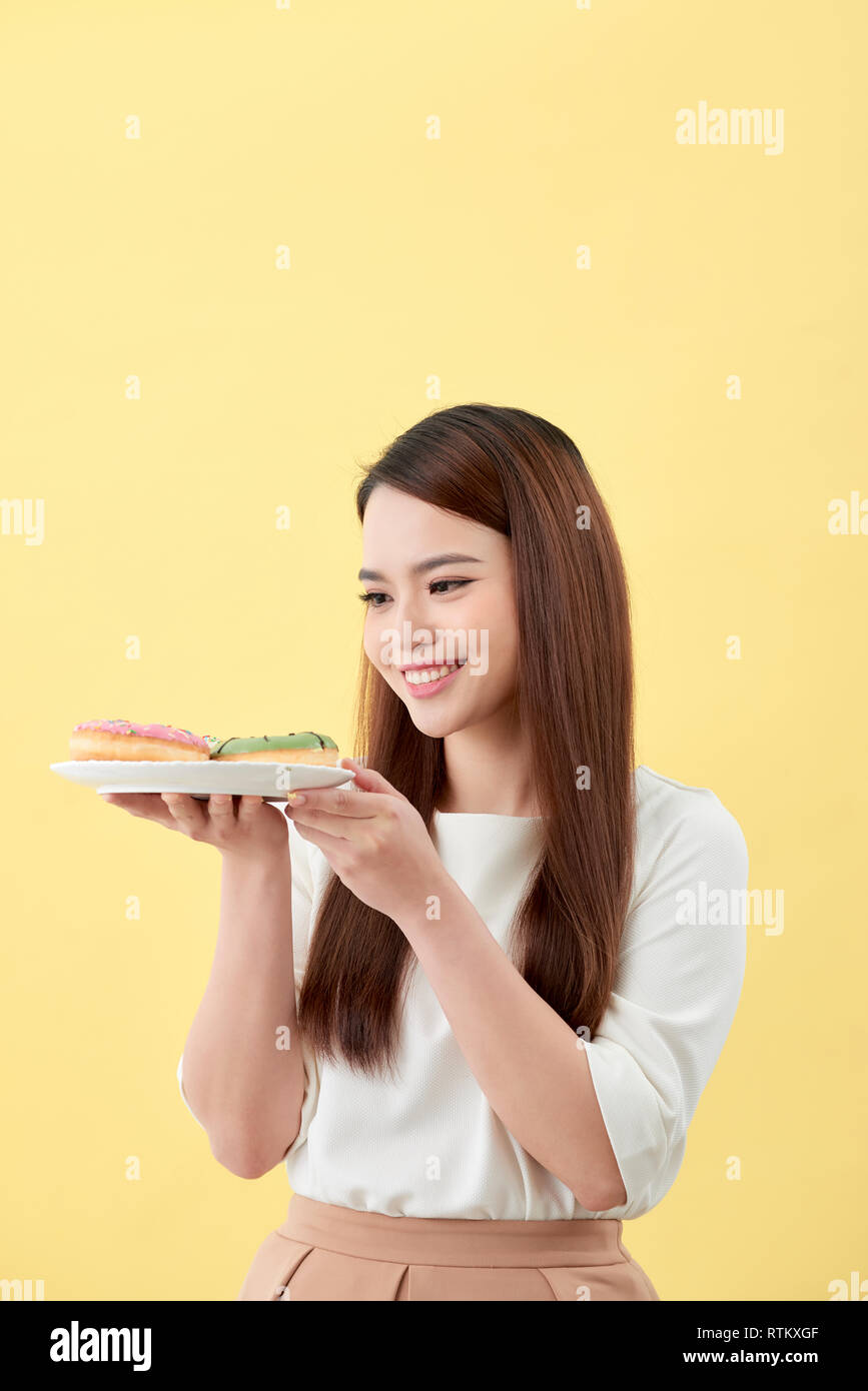 Asian girl show and holding plate full of tasty delicious aromatic donuts in smile face isolated. Stock Photo