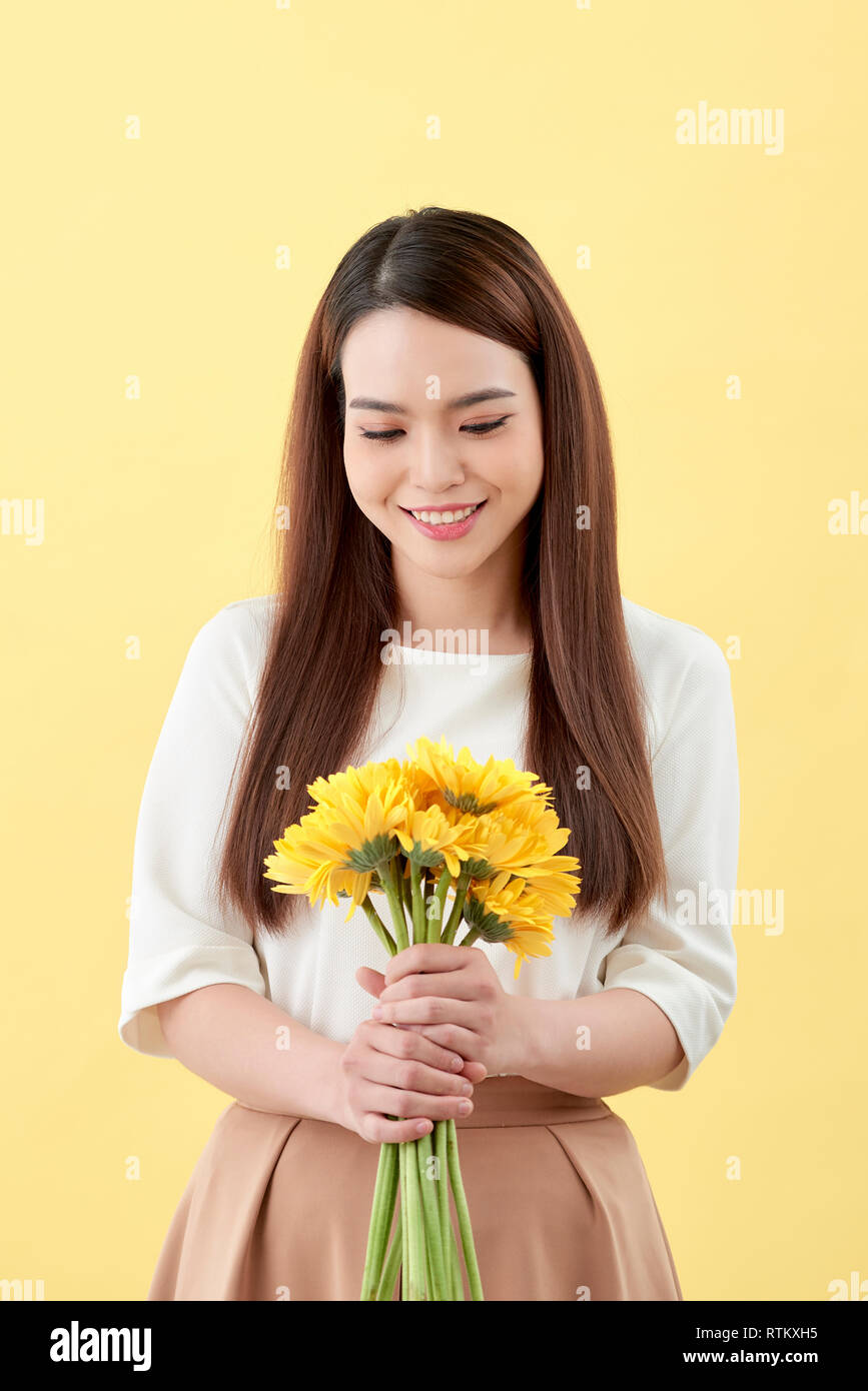 Asian lady holding a bunch of flower standing against a wall Stock Photo