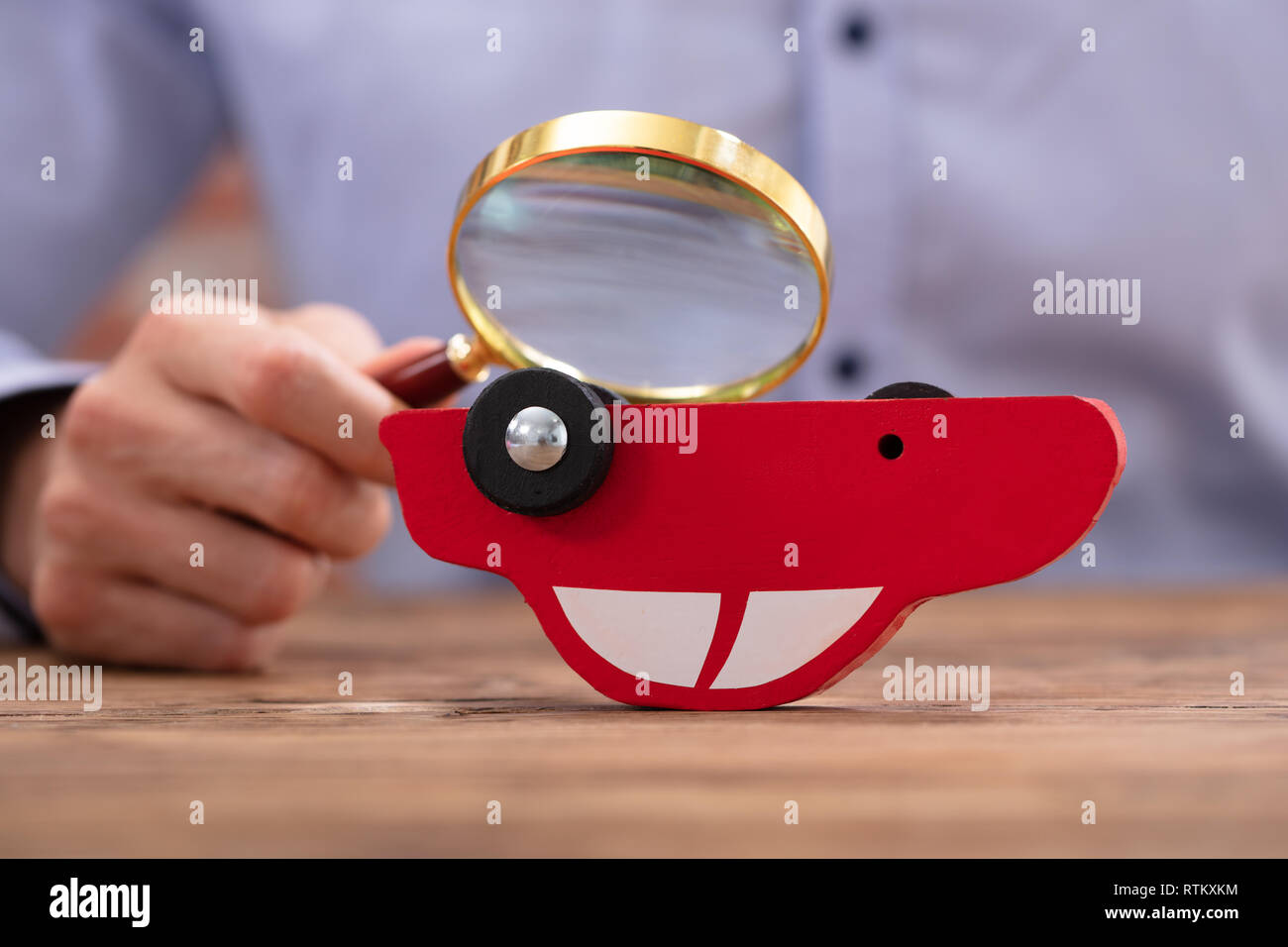Person Scrutinizing A Car Model Using Magnifying Glass On Wooden Desk Stock Photo