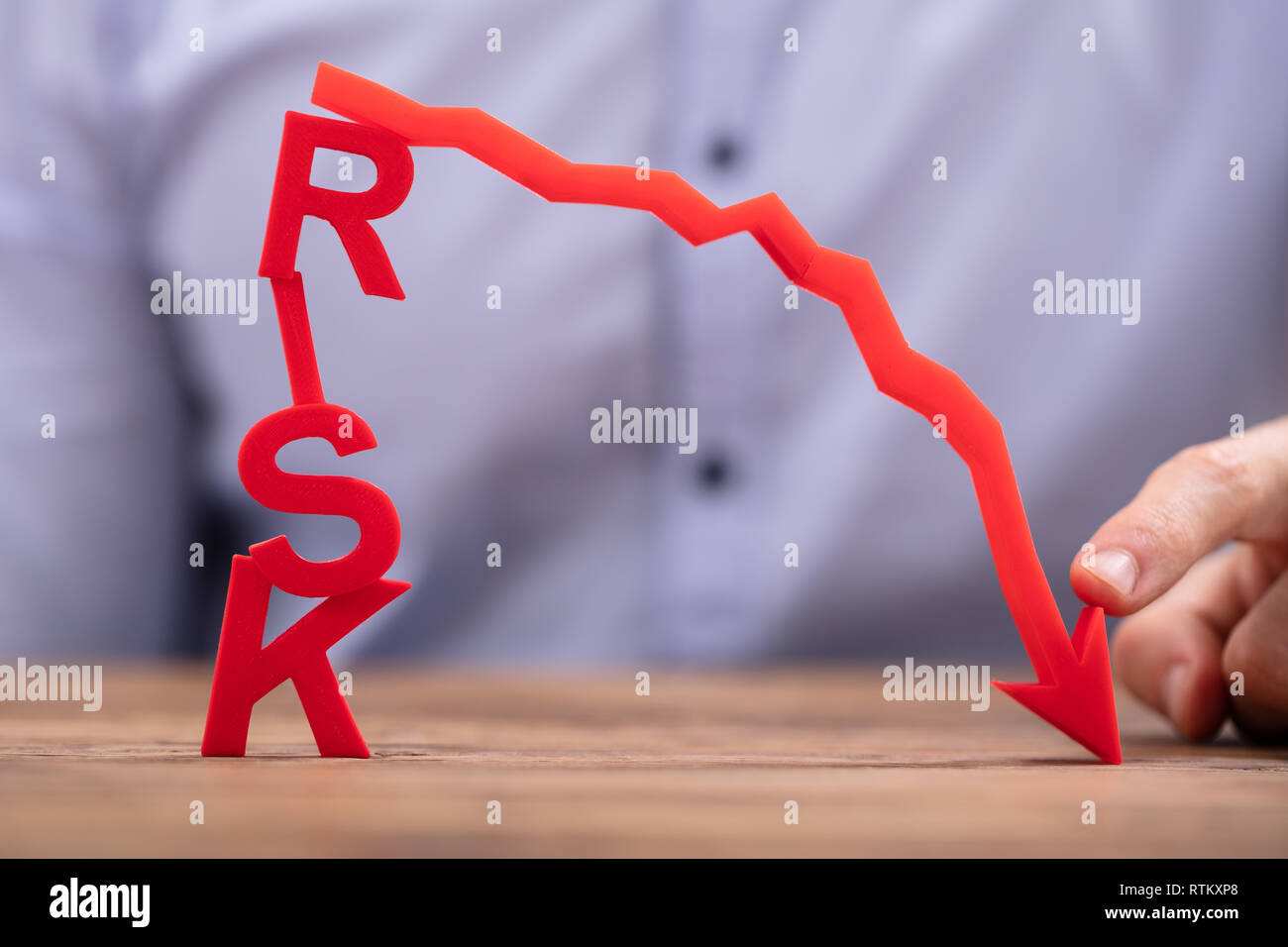 Businessperson Pointing Red Diminishing Arrow Over There Risk Text On Wooden Desk Stock Photo