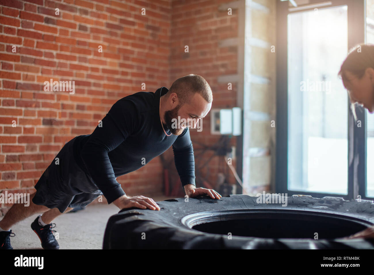 Caucasian crossfit male coach shows crossfit plyometric push-up technique, performed on truck tire to his female trainee , encouraging her with his ow Stock Photo