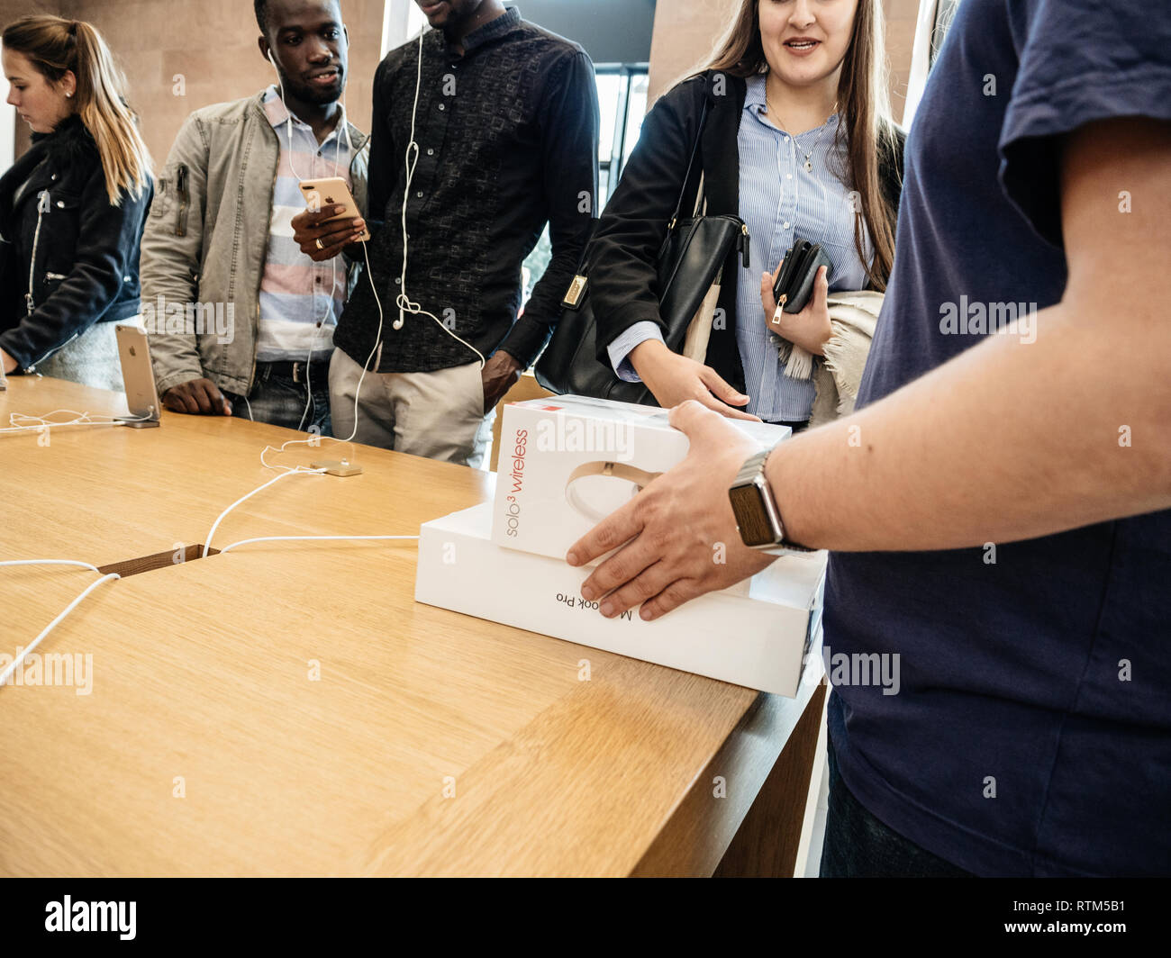 PARIS, FRANCE - SEP 22, 2017: New iPhone 8 and iPhone 8 Plus, as well the updated Apple Watch, Apple TV goes on sale today in Apple Store with young customer student buying Macbook Pro with Beats by dr Dreheadphones Stock Photo