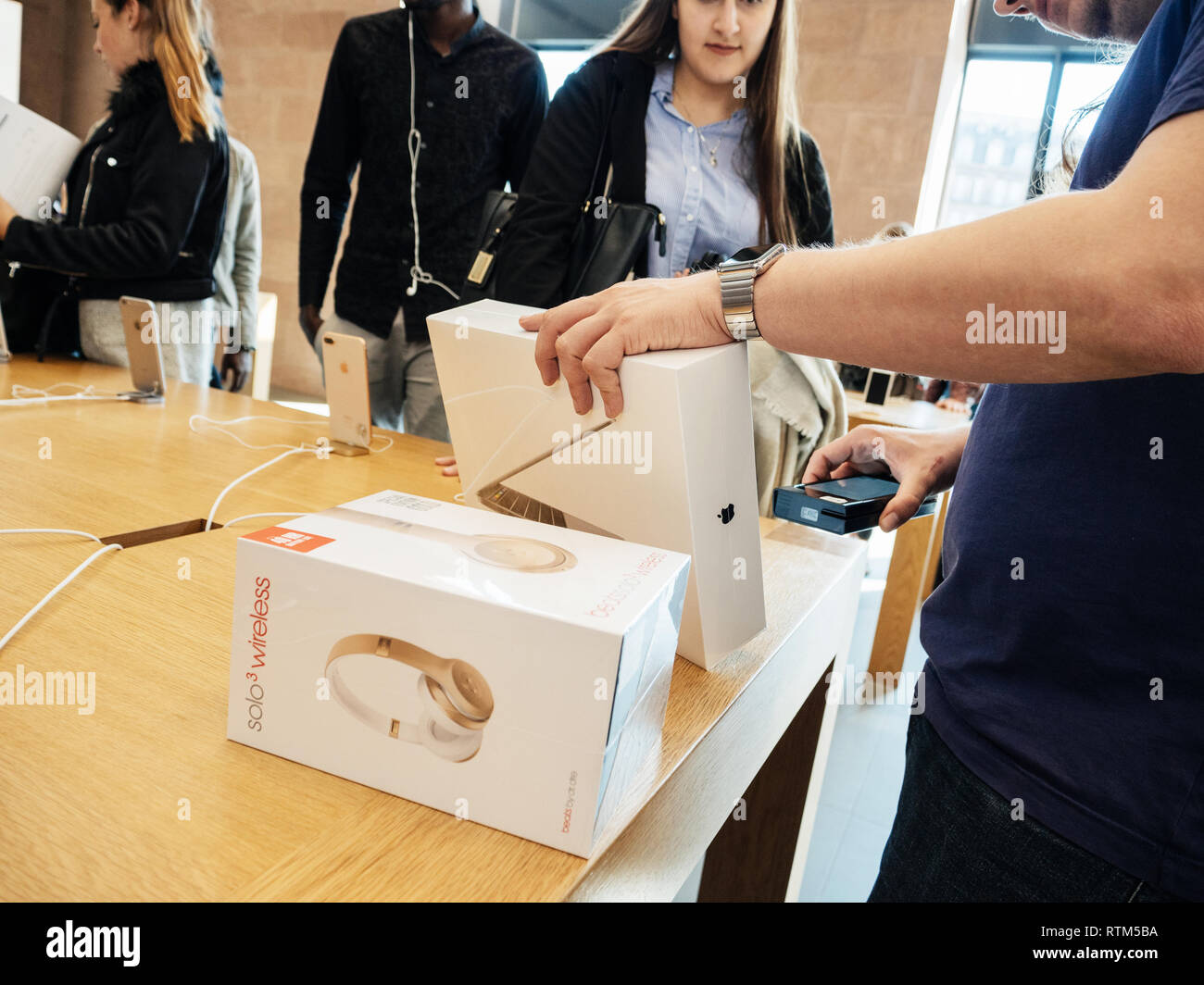 PARIS, FRANCE - SEP 22, 2017: New iPhone 8 and iPhone 8 Plus, as well the updated Apple Watch, Apple TV goes on sale today in Apple Store with young customer student buying Macbook Pro with Beats bu Dr Dre headphones Stock Photo