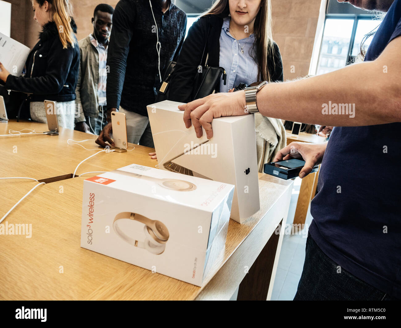 PARIS, FRANCE - SEP 22, 2017: New iPhone 8 and iPhone 8 Plus, as well the updated Apple Watch, Apple TV goes on sale today in Apple Store with young customer student buying Macbook Pro with Beats by dr dre, headphones Stock Photo