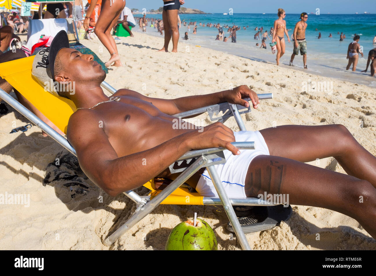 RIO DE JANEIRO - JANUARY 25, 2015: A muscular young Brazilian man lies in a beach chair sunbathing on a bright afternoon on Ipanema Beach. Stock Photo