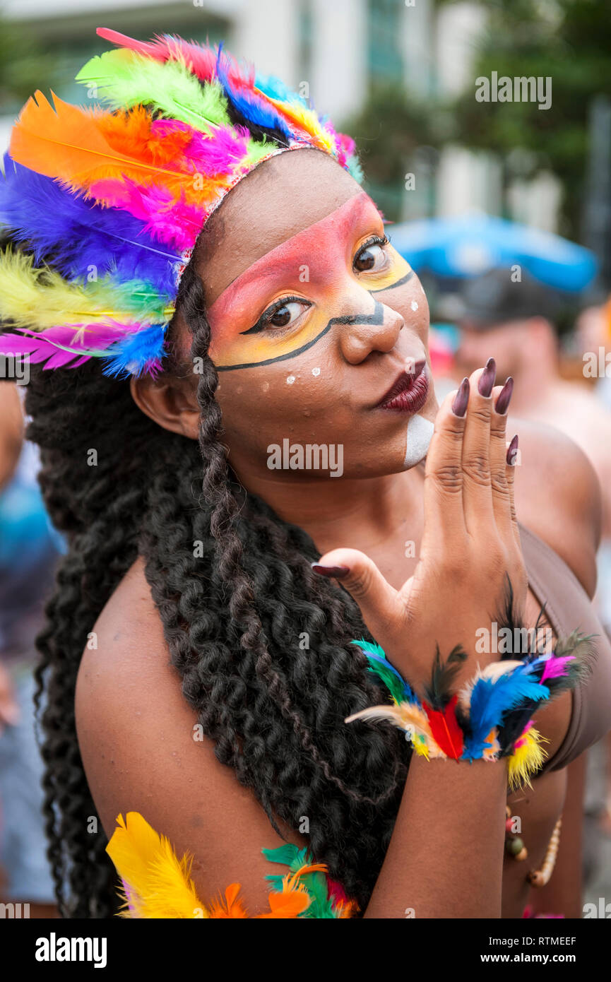RIO DE JANEIRO - MARCH 15, 2017: A young Brazilian woman wearing stylized Native American face paint and feather headdress blows a kiss at Carnival. Stock Photo