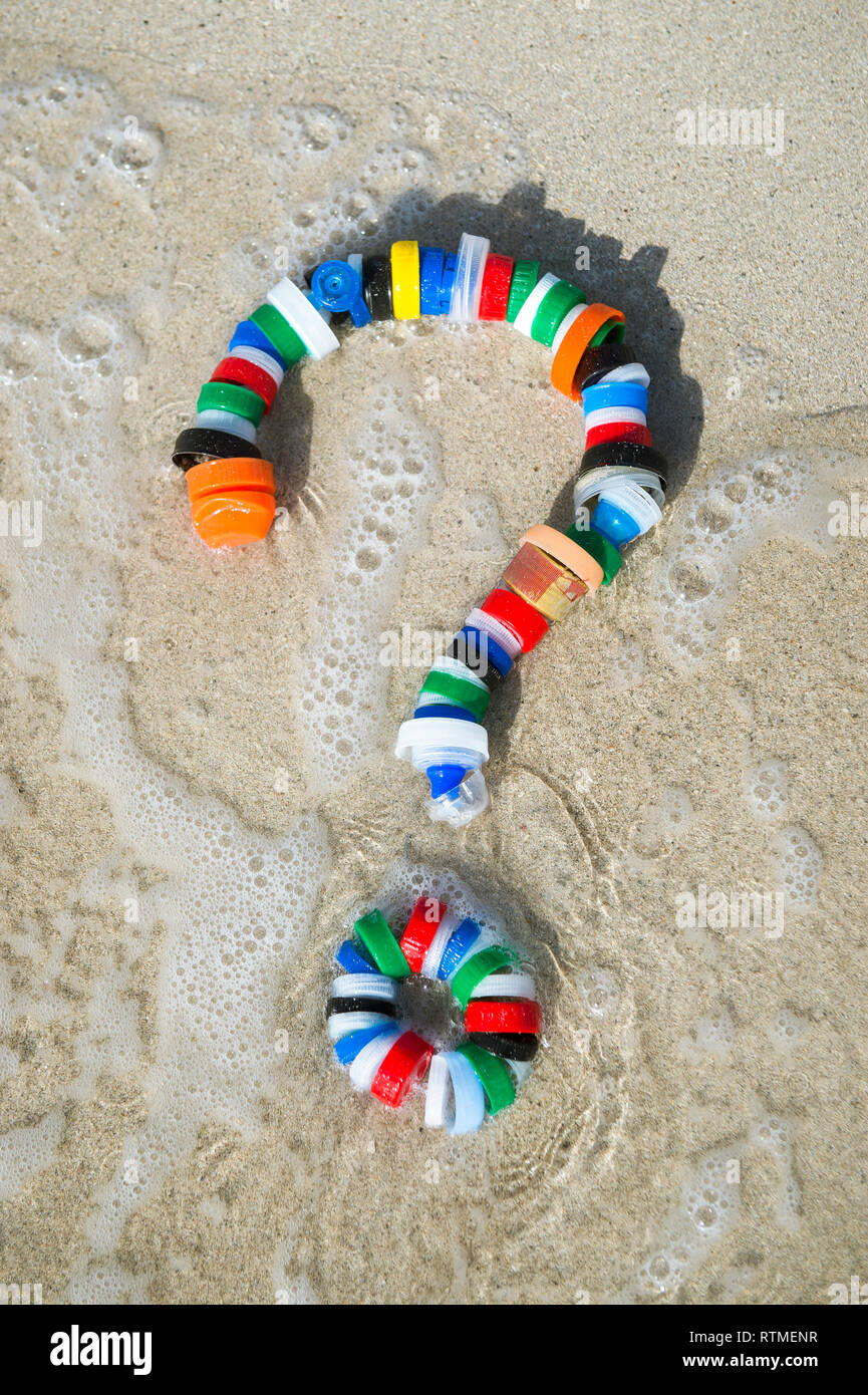 Colorful bottle caps in the shape of a question mark, a reminder for people to reconsider the need for single-use plastic resting on a sandy beach Stock Photo