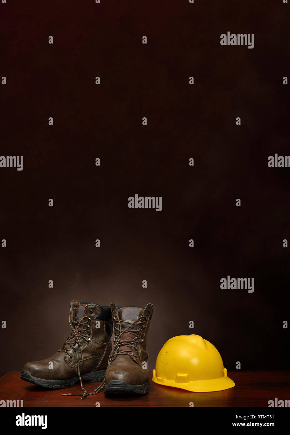 Vertical shot of a pair of brown work boots and a yellow construction helmet on a brown background with copy space. Stock Photo