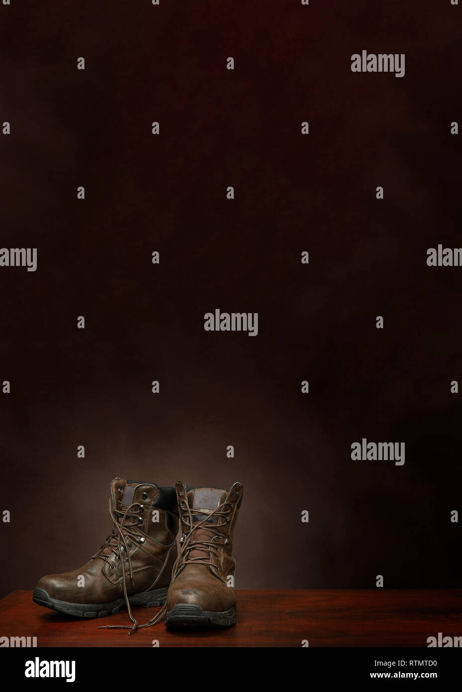 Vertical shot of a pair of old work boots on a brown background with copy space.  The boots are in the lower left hand corner. Stock Photo