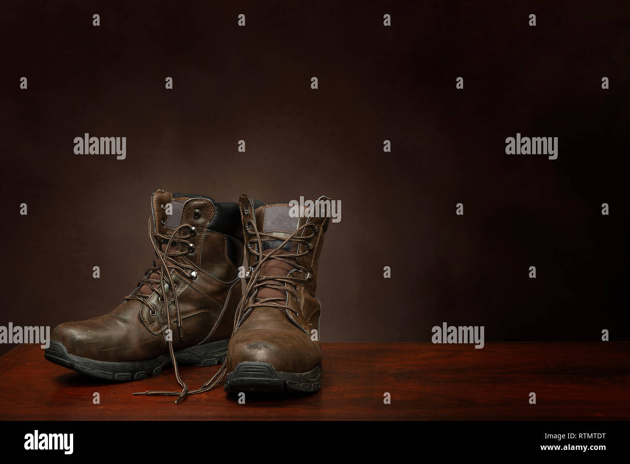 Horizontal shot of a pair of old work boots on a brown background with copy space.  The boots are in the lower left hand corner. Stock Photo
