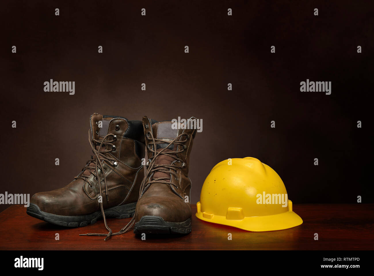 Horizontal shot of a pair of brown work boots and yellow construction helmet on a brown background with copy space. Stock Photo