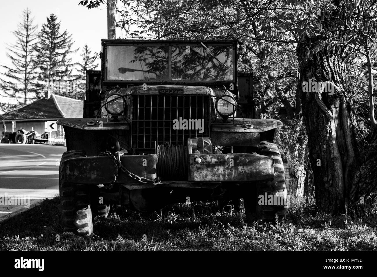An old abandoned military truck, left to rot in the grass, but resisting the tooth of time, large wheels, and corrosive metal.  Black and white Stock Photo