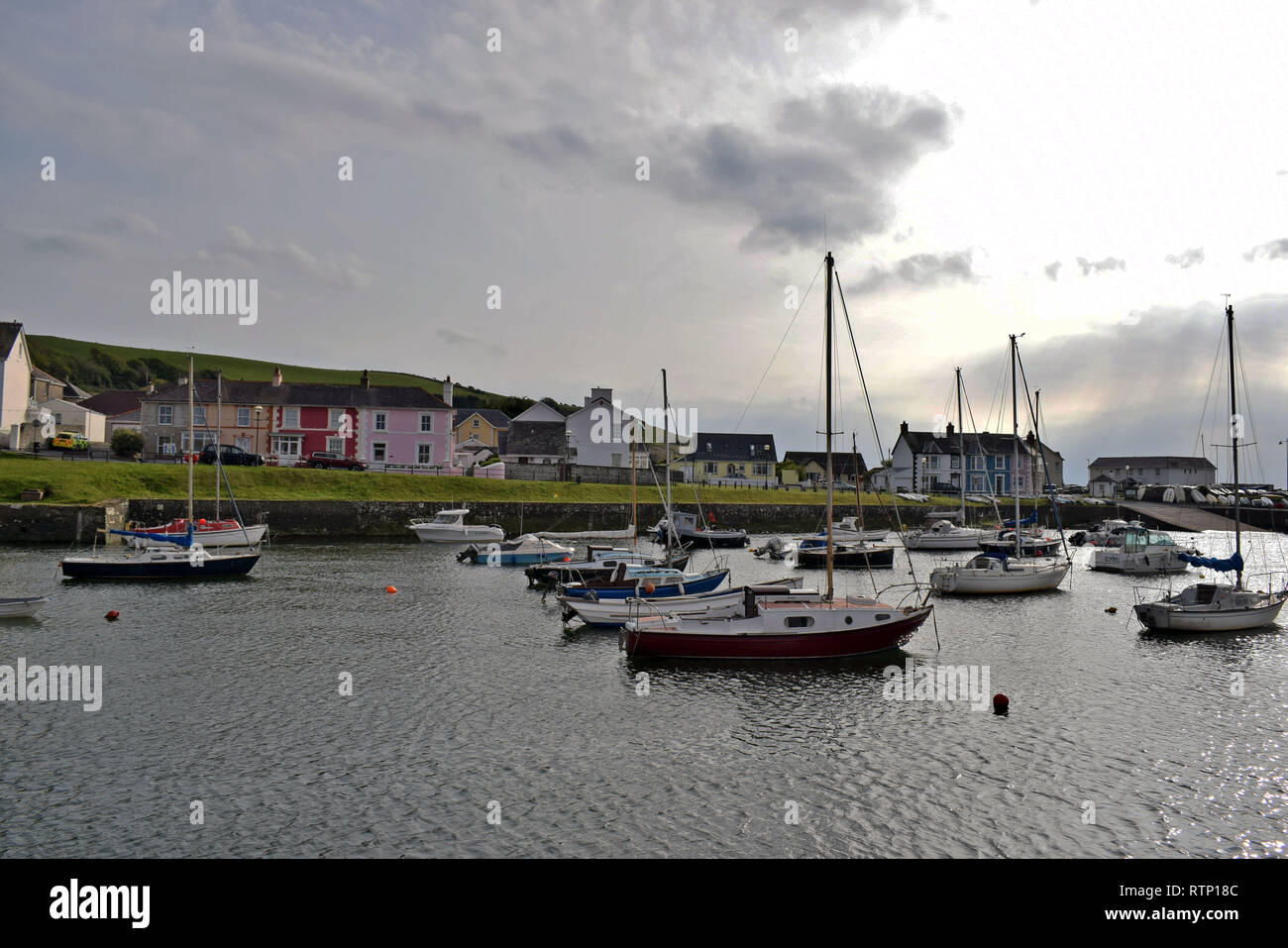 boats on water in the harbour in Wales surrounded by multi coloured houses with a cloudy sky background. Stock Photo