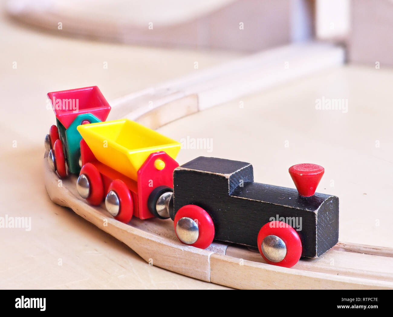 Wooden toy train running on miniature tracks. The black engine pulling colorful cars on the floor. Educational toys for children in preschool and kind Stock Photo