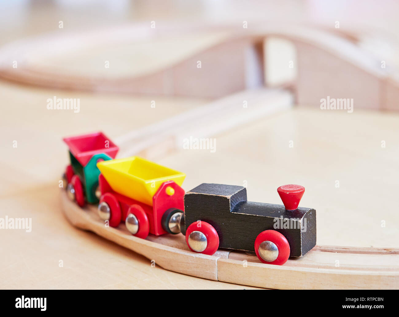 Wooden toy train running on miniature railway tracks. The black engine pulling colorful cars on the floor. Educational toys for children in preschool  Stock Photo